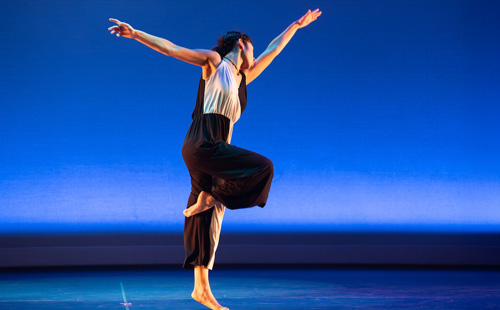 A dancer on stage with outstretched arms in front of a blue background