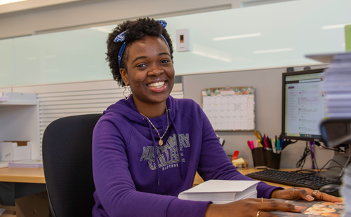 Denisia Akagah sitting at a desk smiling